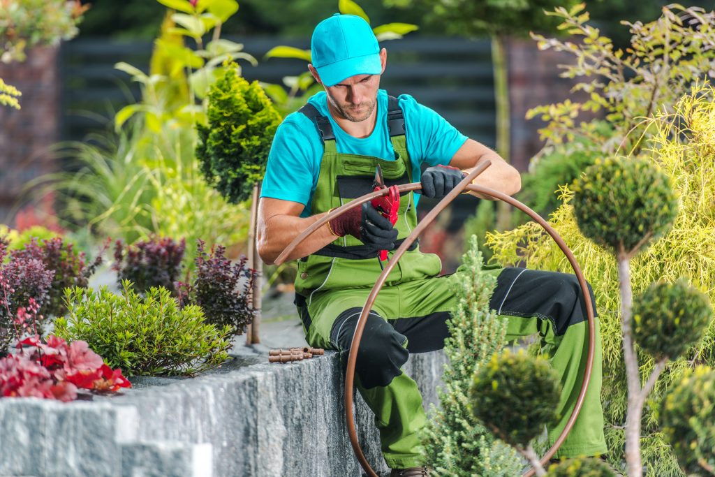 Bild eines Gartenlandschaftsbauer der im Blumenbeet sitzt und Draht schneidet.