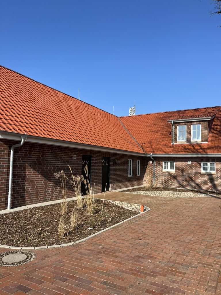 Zwei Beete mit Mulch und Pflanzen vor einer Hauswand.